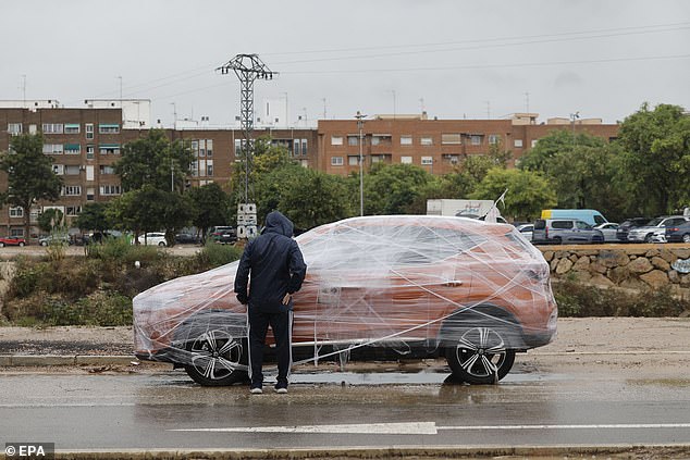 A passerby observes a vehicle wrapped in plastic in Catarroja municipality, Valencia, Spain, 09 October 2025 as the region is on high alert due to Storm Alice