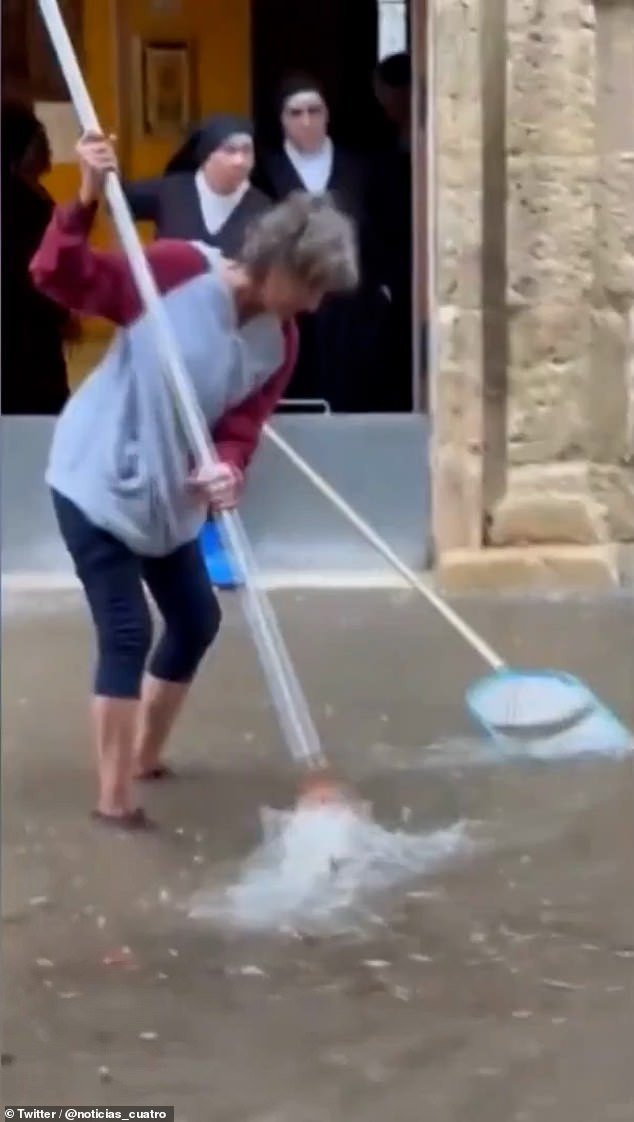 A volunteer is seen cleaning a flooded street