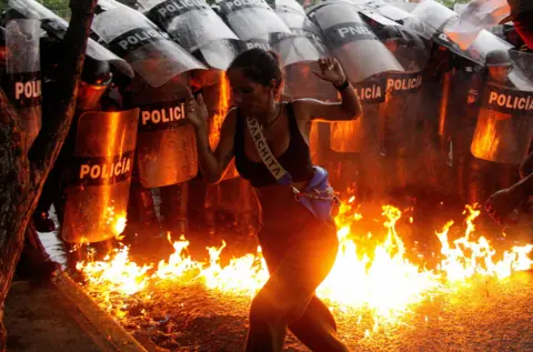 Reuters A woman runs in front of riot police, with flames on the road, during a protest in Venezuela in July, following Nicolas Maduro claiming victory in the presidential election. 