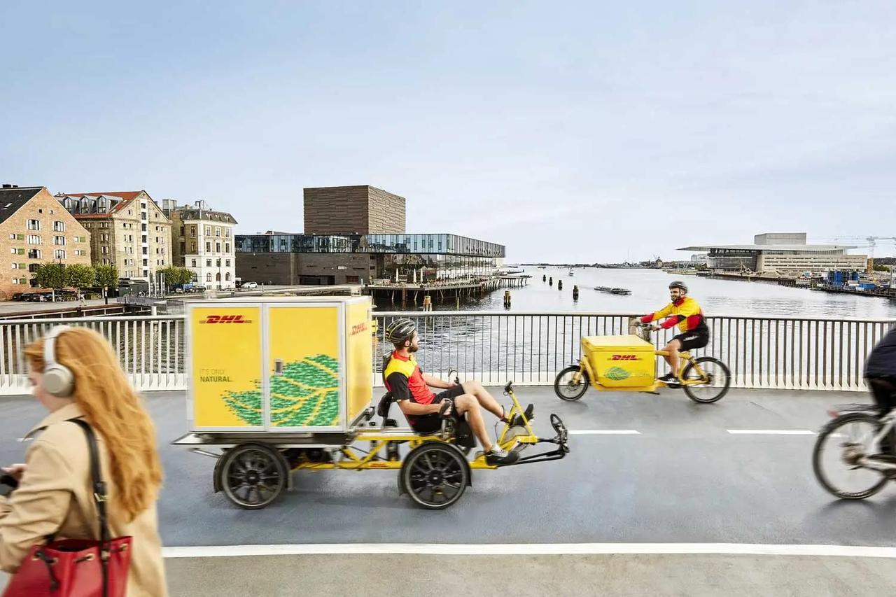 DHL Express couriers ride electric-assisted cargo bikes over a bridge in central Copenhagen as part of the company’s zero-emission delivery initiative. (Photo via Great Place To Work)