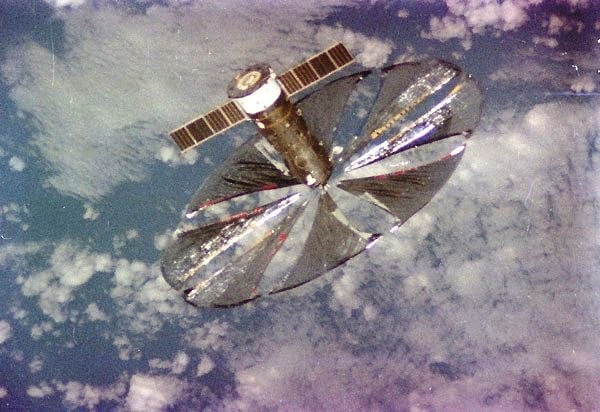 A grainy image of a satellite with circular, shiny material deployed. 