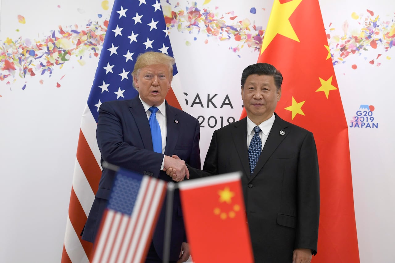 Two men in suits shake hands in front of the flags of the U.S. and China.