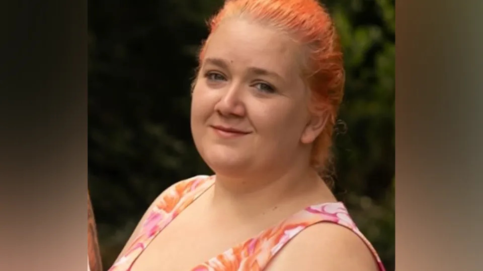 A close up photo of Rhiannon Whyte, showing her with orange-dyed hair and a multi-coloured vest-type top.