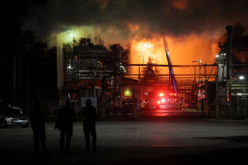 People stand nearby as firefighters work to contain a large fire that broke out at the Chevron refinery in El Segundo, California, on Thursday.