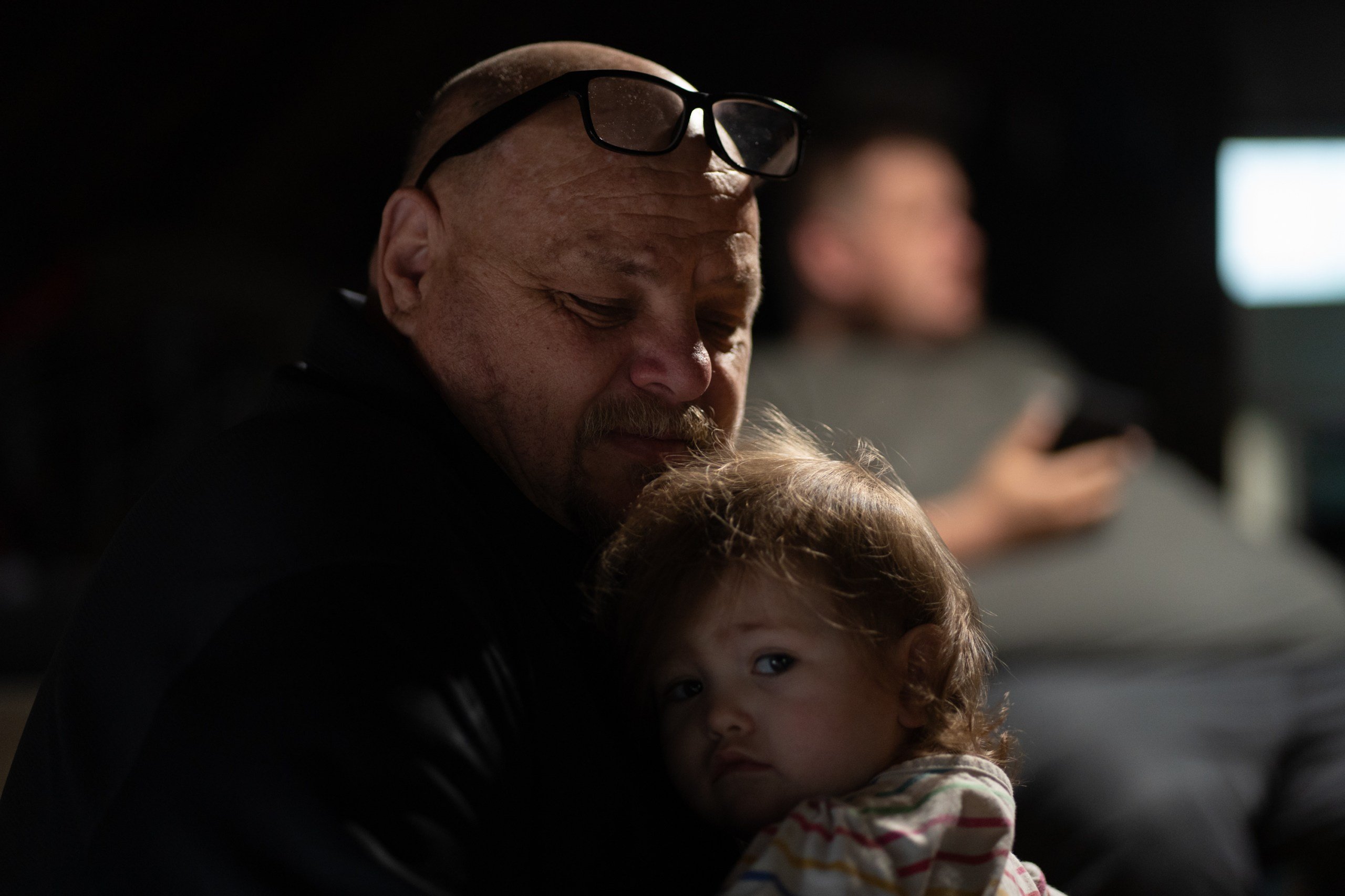 A little girl rests on the chest of a man who has glasses propped on his head.