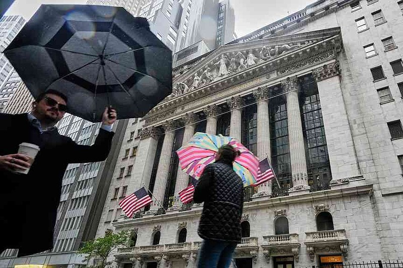 People with umbrellas pass the New York Stock Exchange, Monday, Oct. 13, 2025. (AP Photo/Richard Drew)