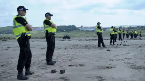 Getty Images A string of 15 uniformed police officers spread across a beach. In the far distance we can see the Trump Turnberry Hotel.