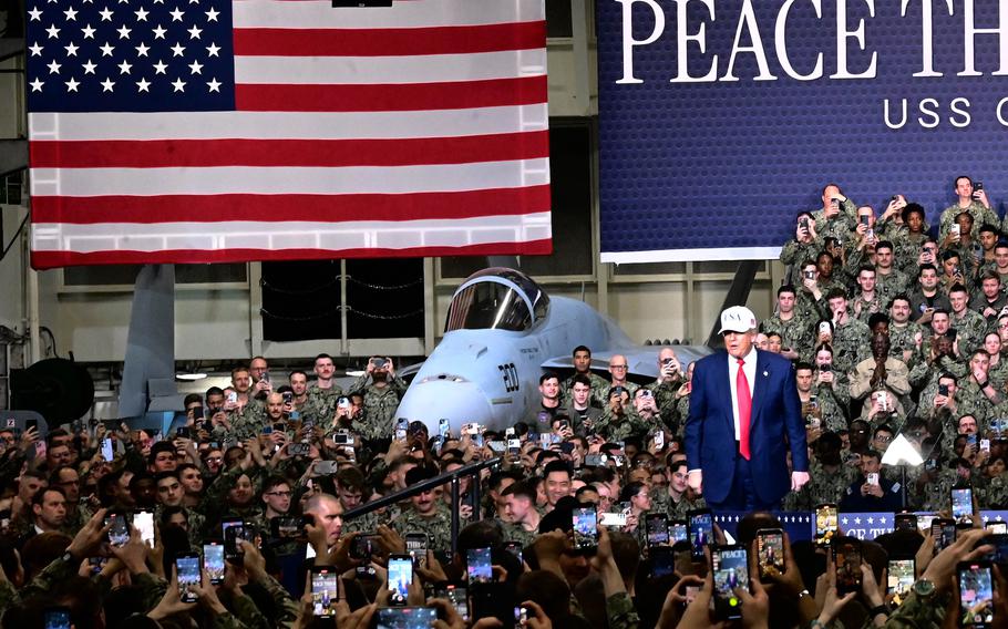 President Donald Trump stands on a stage in front of Navy sailors.