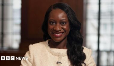 Afua Kyei wears a white suit jacket with a beaded trim. She has long dark hair and is smiling.