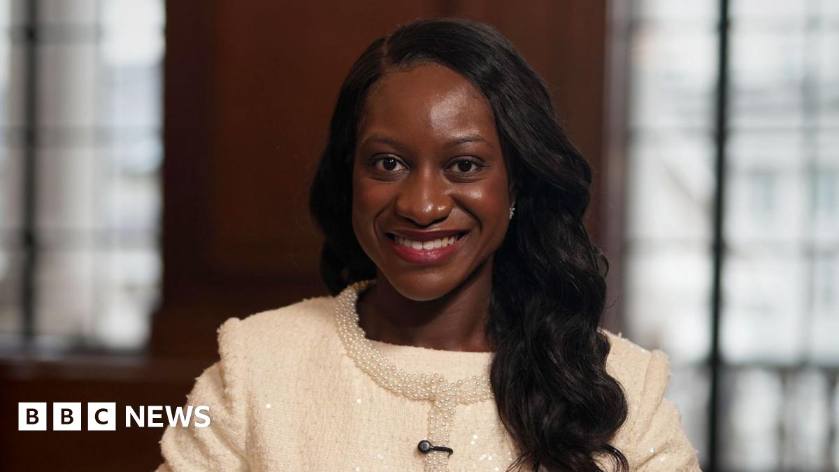 Afua Kyei wears a white suit jacket with a beaded trim. She has long dark hair and is smiling.