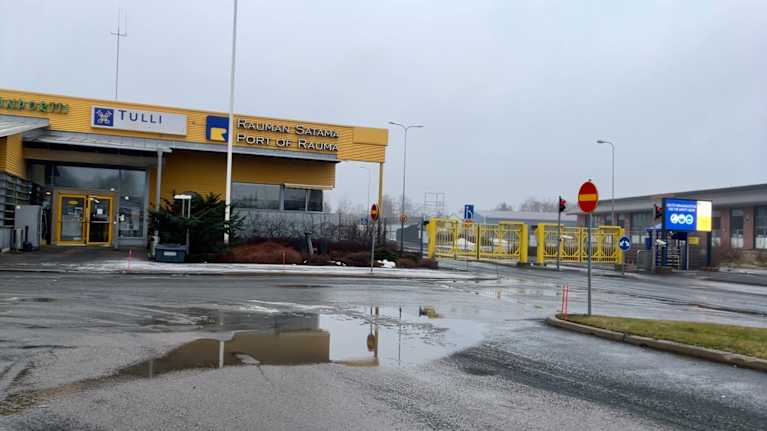 A low yellow building with a sign saying Port of Rauma and Tulli (Customs) with a puddle in the foreground.