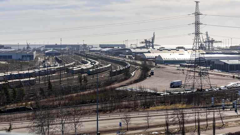 A view from above of an extensive port transit hub with trees, power lines, buildings, trains and a lorry.
