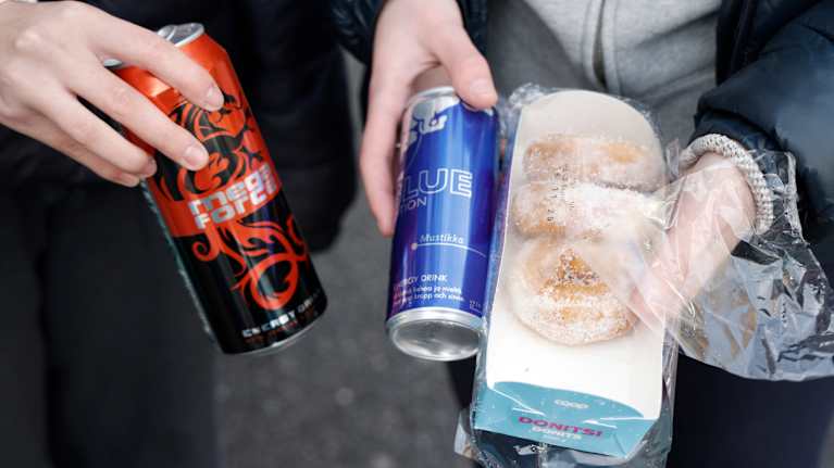 Tyttöjen kädessä energiajuomatölkkejä ja donitsipakkaus.