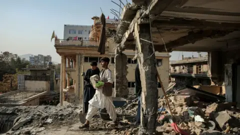 EPA Two young men, one in all black holding a spade and another in white carrying a brick, stand amid the rubble of a destroyed building in Kabul