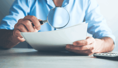 A man holds a magnifying glass over a contract.