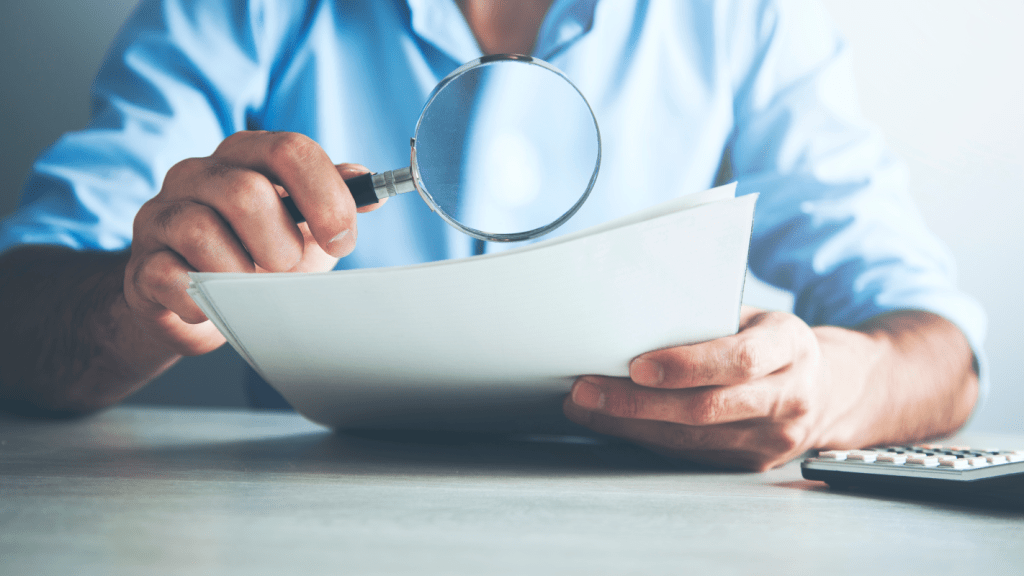 A man holds a magnifying glass over a contract.