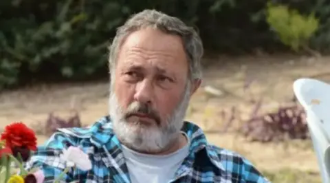 Hostages and Missing Families Forum Eliyahu Margalit in a blue shirt sat near flowers outside