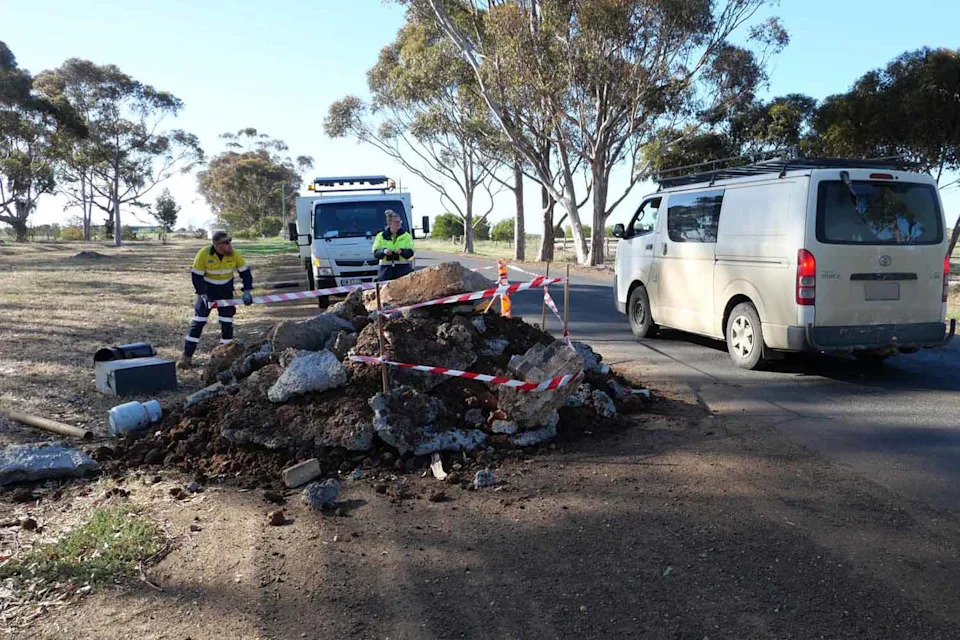 A pile of illegally dumped waste on the side of a road with council workers standing beside it.