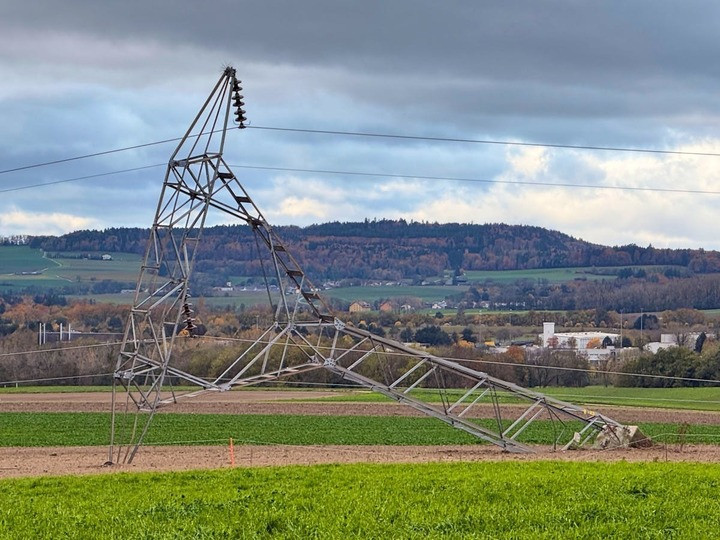 Ein umgestürzter Strommast auf einem Feld mit Hintergrund von Hügeln und bewölktem Himmel.