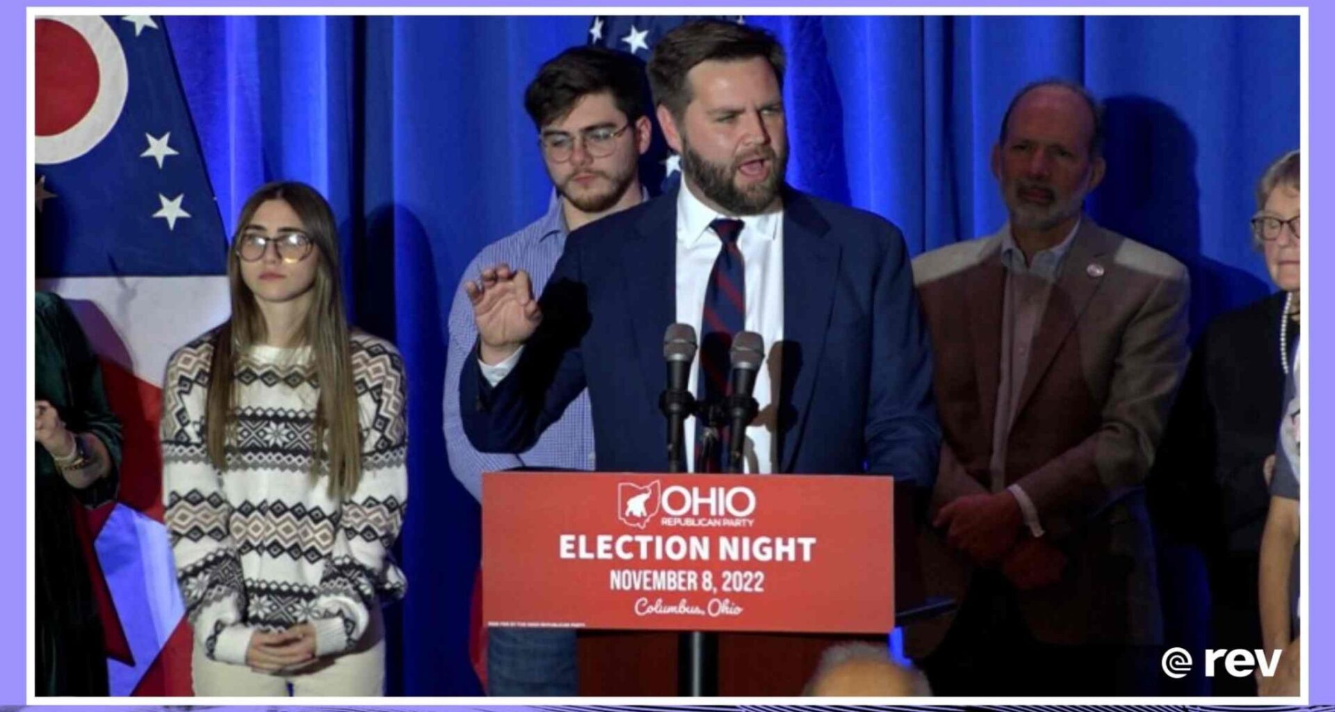 J.D. Vance speaks at a podium with a crowd behind him.