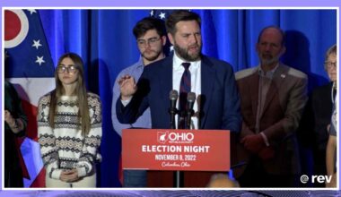 J.D. Vance speaks at a podium with a crowd behind him.