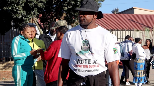 Man wear dark sun hat and T-shirt wey say "Vote Operation Dudula, Mass Deportation".