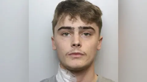 West Yorkshire Police Police mugshot of Alfie Franco, with brown wavy air and a moustache. He has a white bandage on the right side of his neck.
