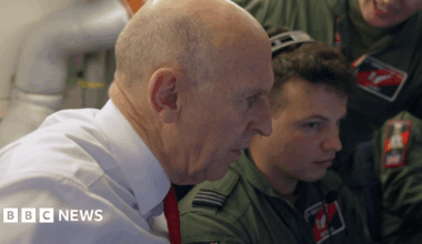 Defence Secretary John Healey in side profile, wearing a white shirt and red tie, alongside RAF crew in uniform