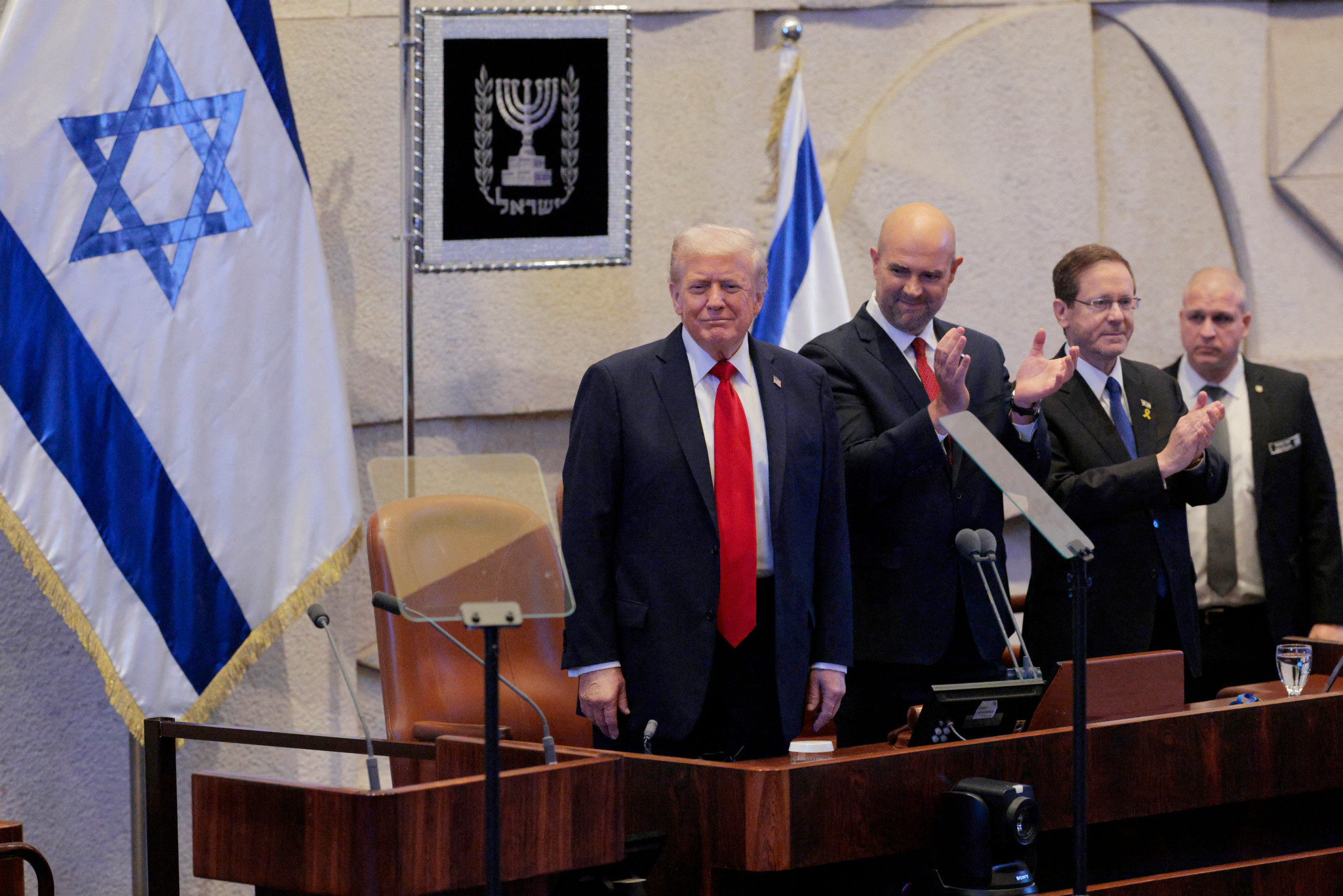 Le président américain Donald Trump reçoit une ovation debout au parlement israélien, la Knesset, à Jérusalem, aux côtés du président de la Knesset Amir Ohana et du président israélien Isaac Herzog, le 13 octobre 2025, après un accord de cessez-le-feu avec le Hamas.