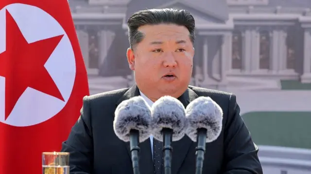 Kim Jong Un speaking into three large microphones at a podium