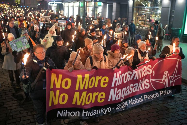 people hold a banner that says no more Hiroshimas, no more Nagasakis