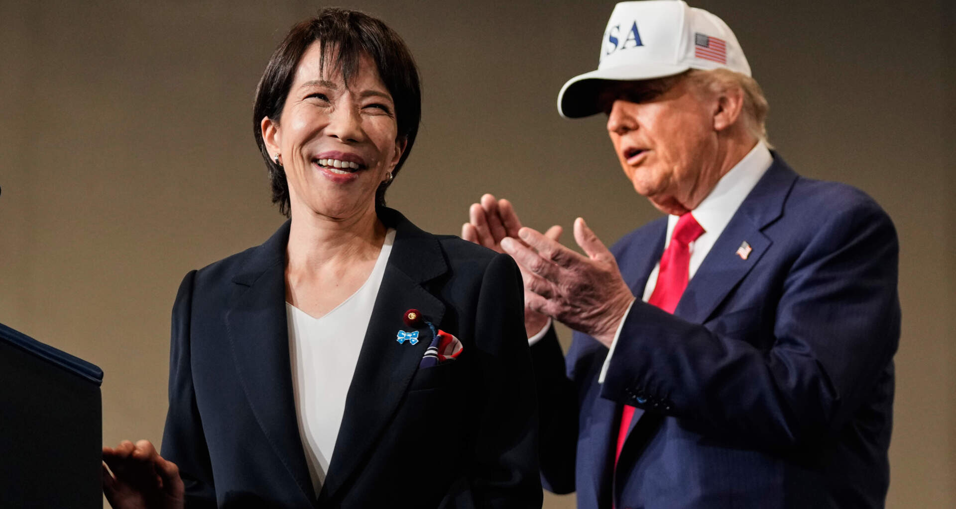 Japanese Prime Minister Sanae Takaichi, with President Donald Trump, reacts as she was speaking to members of the military aboard the USS George Washington, an aircraft carrier docked at an American naval base, in Yokosuka, Tuesday, Oct. 28, 2025. (Mark Schiefelbein/AP)