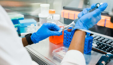 Close-up, the hands of a MD/PhD student, Courtney A. Swain (Graduate Student, Cancer Biology) are wearing blue PPE gloves while using a pipette in performing cancer research in the Shevde-Samant Lab, June 2022.