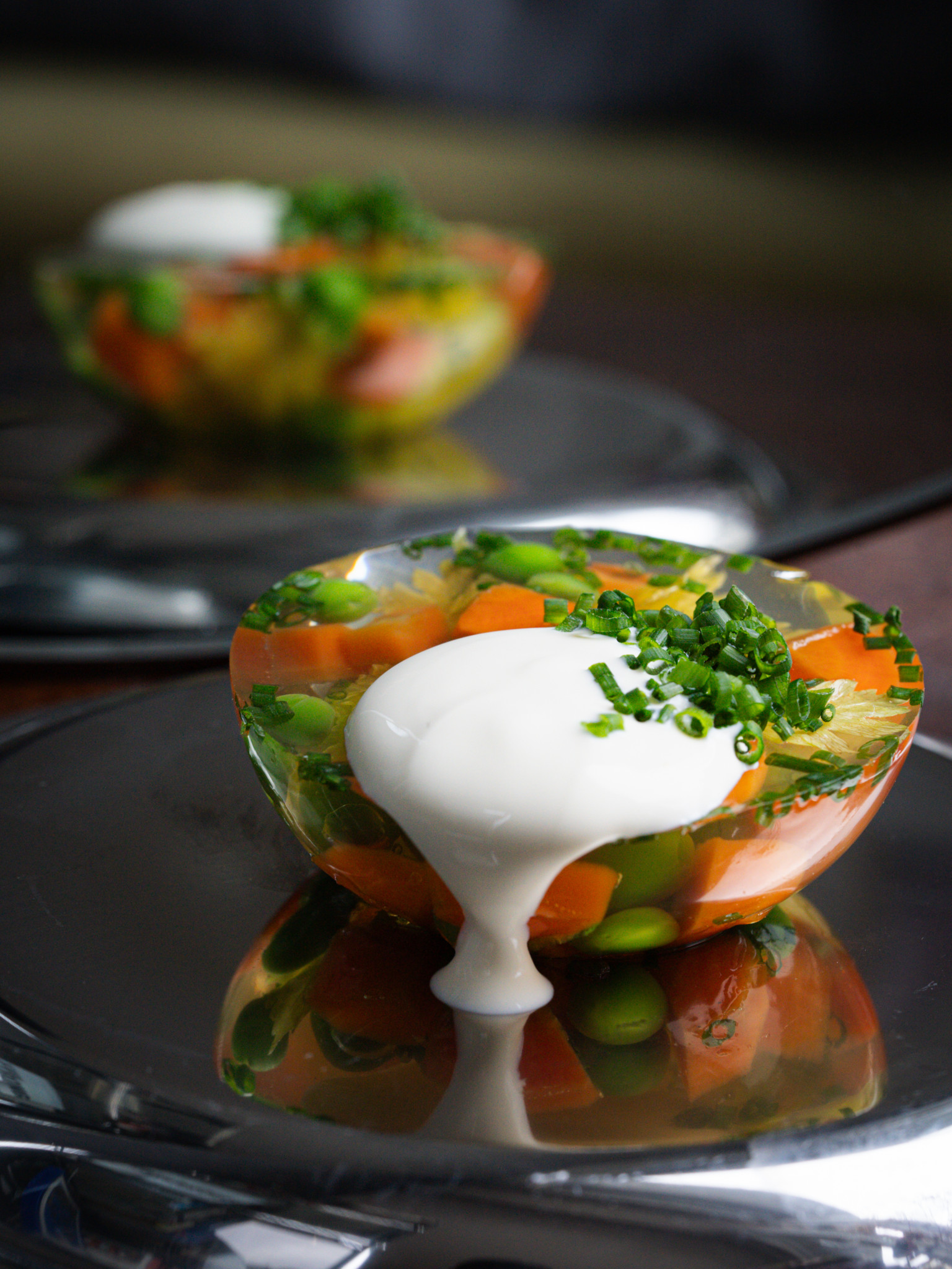 Une gelée colorée de légumes avec une garniture de crème et de ciboulette sur une assiette en métal. Une gelée colorée de légumes avec une garniture de crème et de ciboulette sur une assiette en métal.
