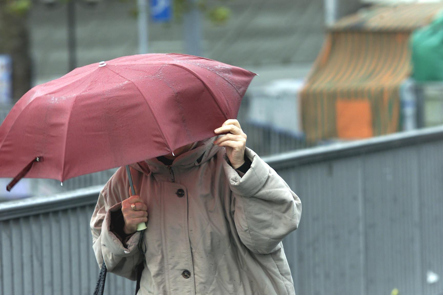 Eine Person mit einem roten Regenschirm schützt sich vor starkem Regen.