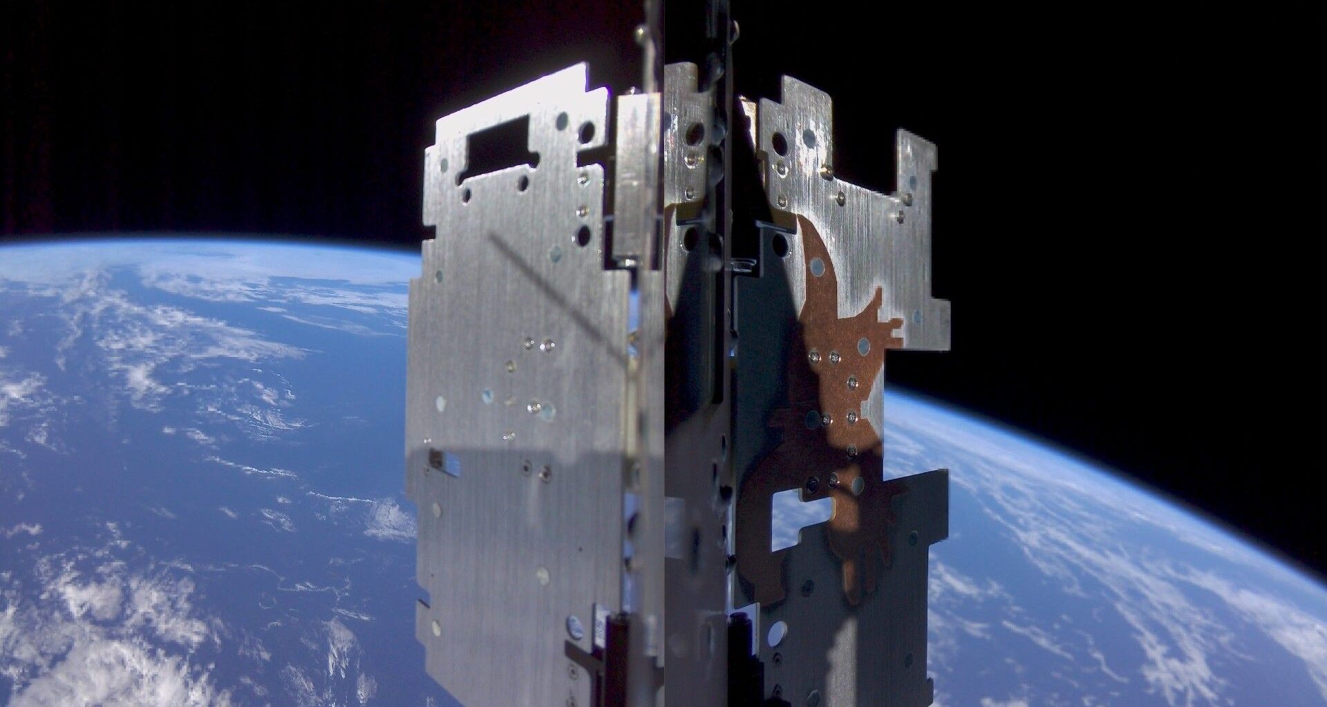 a metal cube-shaped device in the foreground with a blue-and-white earth in the background