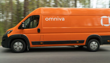 An orange delivery van with Omniva written along the side drives down a tree-lined road