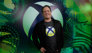 Phil Spencer standing in front of Xbox logo wall wearing a t-shirt with the Xbox symbol.