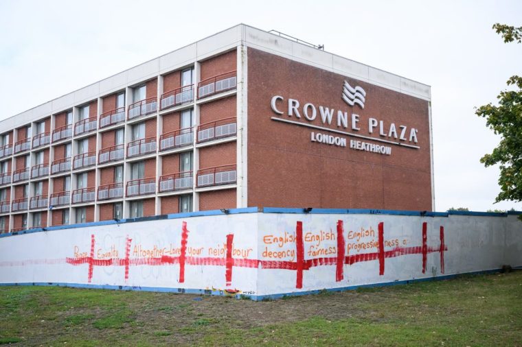 WEST DRAYTON, ENGLAND - SEPTEMBER 02: Positive messages are seen overlaid on St. George's flag graffiti at the Crowne Plaza London Heathrow Hotel on September 02, 2025 in West Drayton, England. The perimeter fence of the hotel, which has hosted migrants for several years, has been recently covered in competing layers of messaging relating to migration. Last week, the Court of Appeal overturned a temporary injunction that would have seen asylum-seekers removed from the Bell Hotel in Epping, which has sparked further protests by anti-immigration campaigners, including a demonstration that took place last weekend outside the Crowne Plaza. The government's policy of housing asylum applicants at hotels around England has been the subject of a wave of protests in recent months. (Photo by Leon Neal/Getty Images)