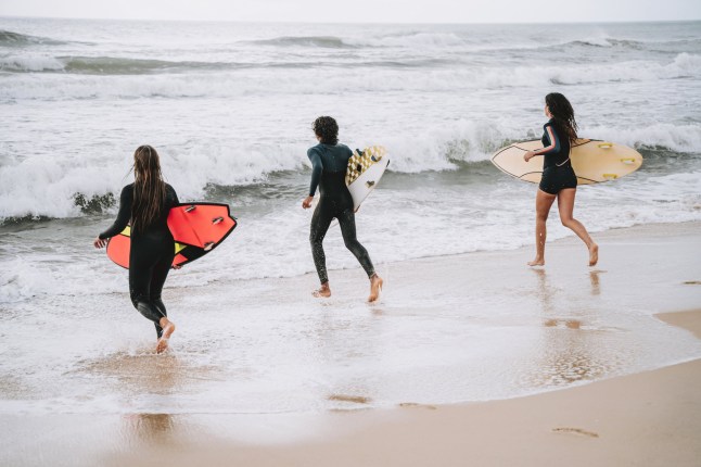 Group of three friends running to surf in the sea