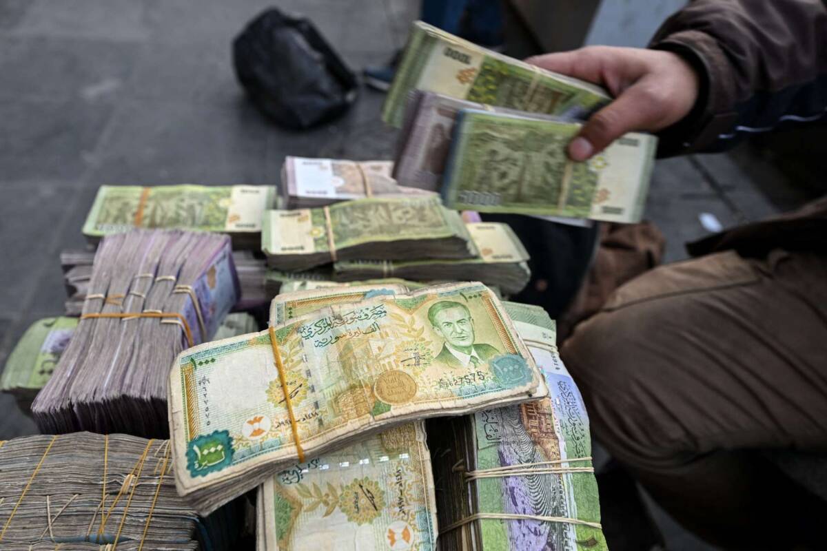 A currency trader sits by a stack of Syrian pounds at his street stall in Damascus, 14/1/2025 (Louai Beshara/AFP)