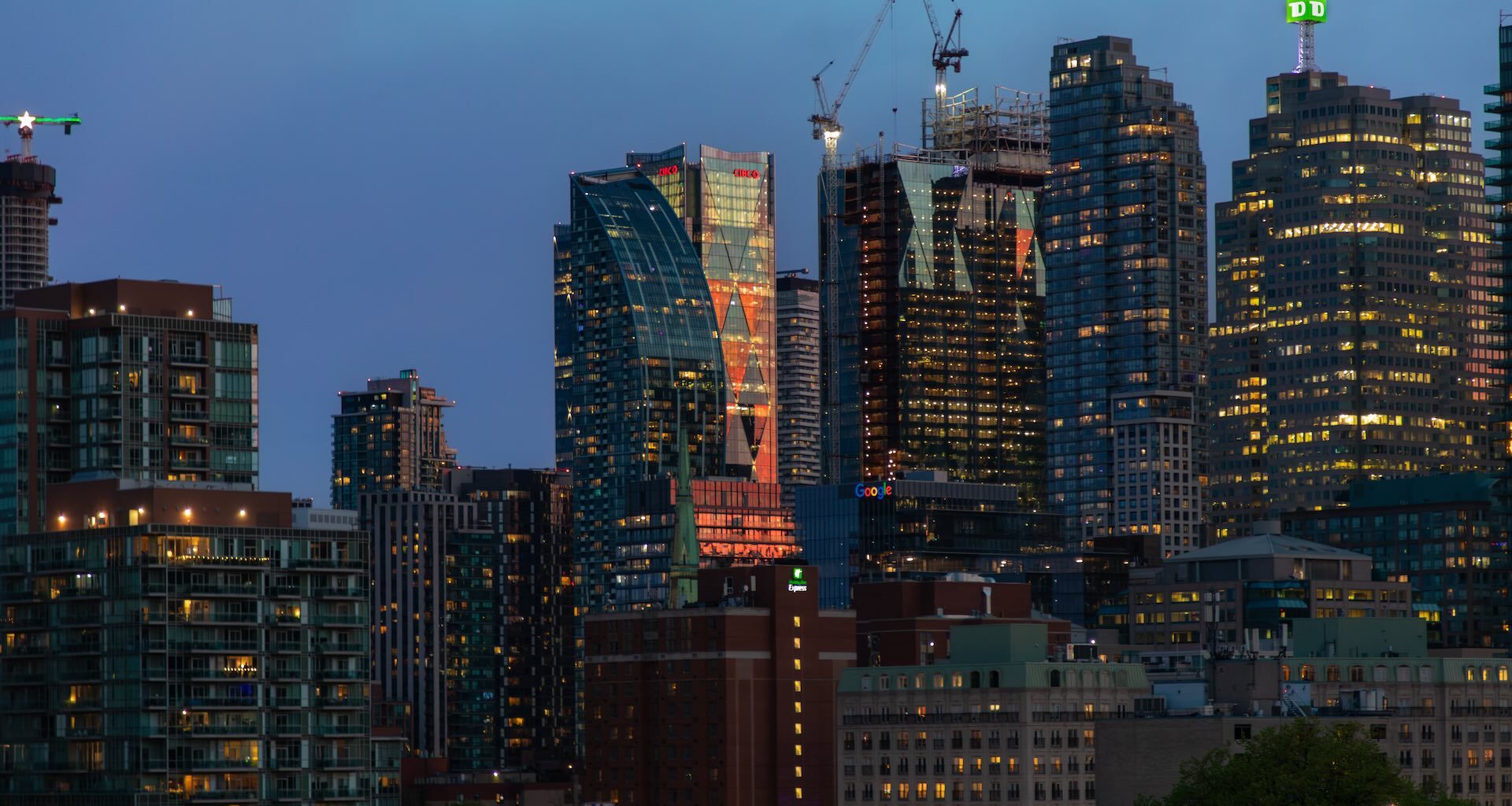 Image of the Toronto skyline with construction cranes rising above some buildings.
