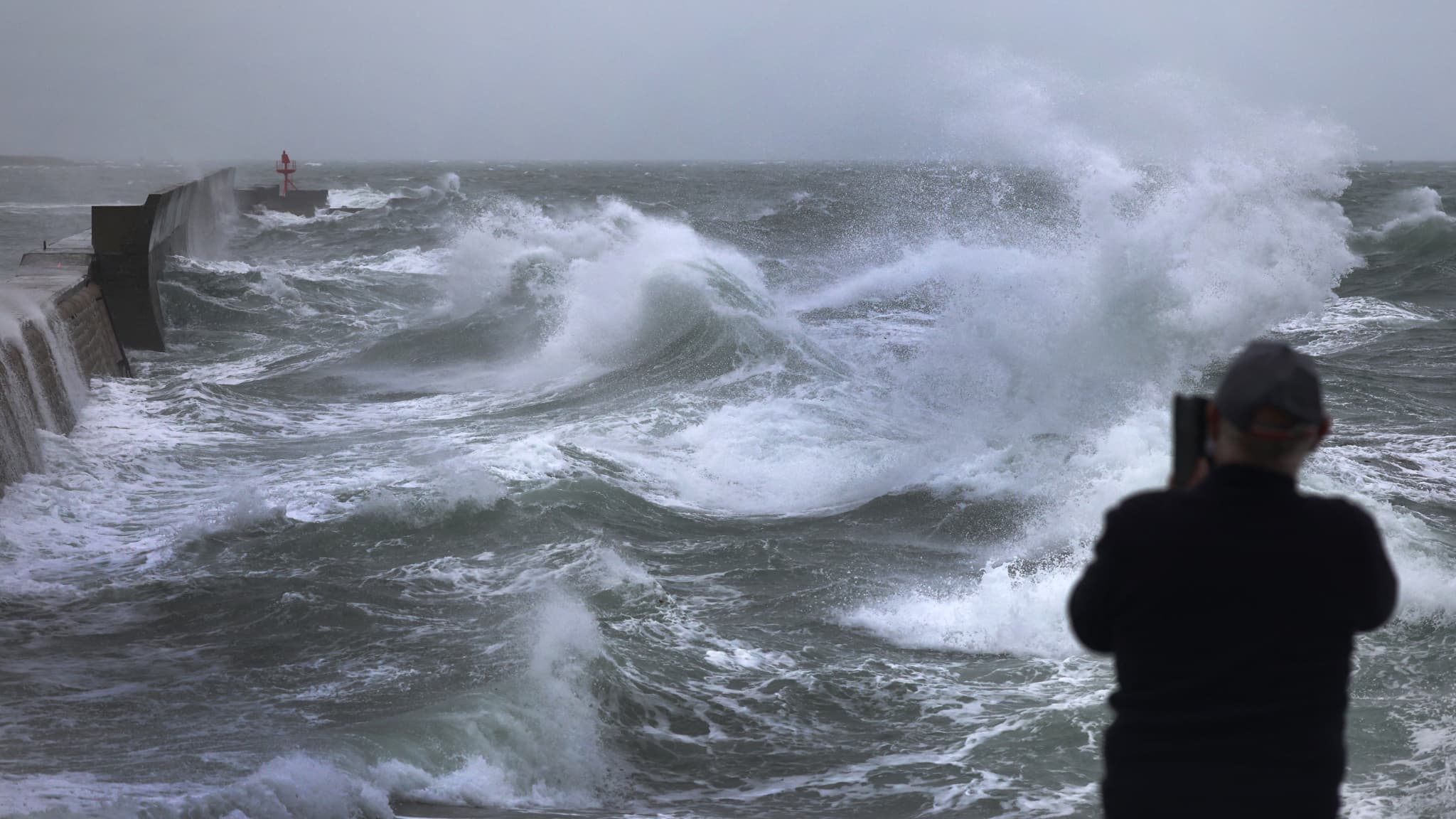 Un homme prend une photo avec son smartphone alors que d'énormes vagues et des vents violents causés par la tempête Benjamin frappent le port de Plobannalec-Lesconil, dans l'ouest de la France, le 22 octobre 2025.