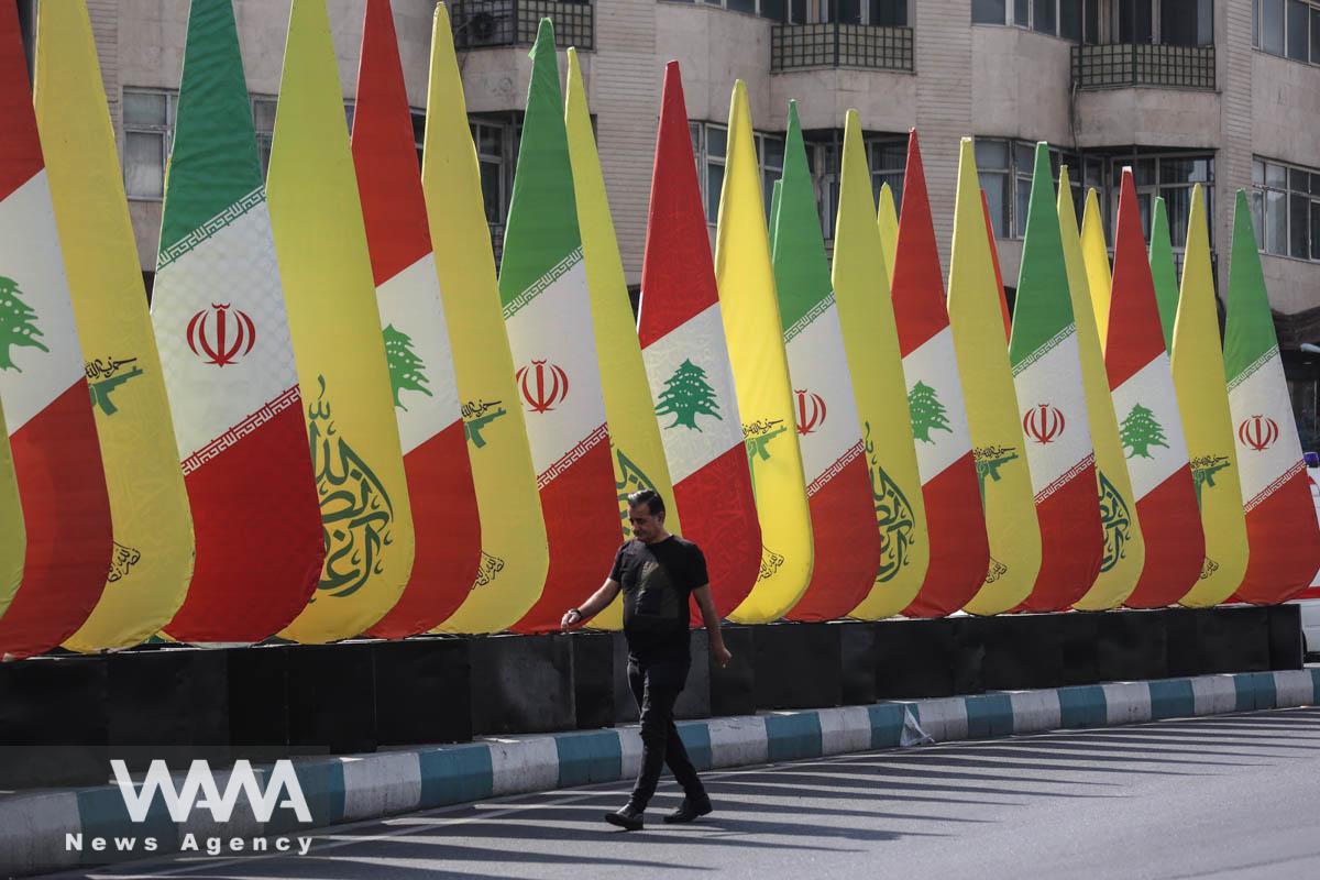 An Iranian man walks next to the stands with the flags of Iran, Hezbollah and Lebanon in a street