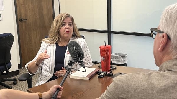 Dianna Valles, president of the Culinary Workers Union Local 226 in Las Vegas, Nevada, sits at a wooden conference table speaking with David Brancaccio, a microphone held in front of her face.
