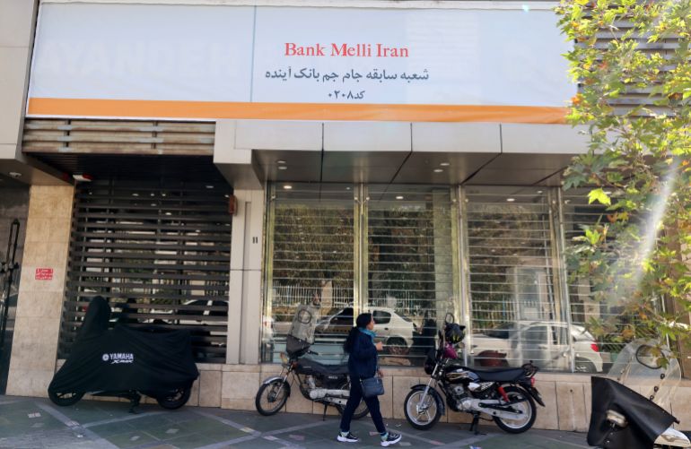 An Iranian woman walks past a branch of the state-owned Melli Bank, which absorbed the assets of the now-defunct Ayandeh Bank, with signage on its facade reading in Farsi "This former Ayandeh Bank branch is now part of Melli Bank", in the capital Tehran on October 25, 2025.