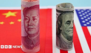 Banknotes from China and US are rolled up and standing upright on flags of both countries