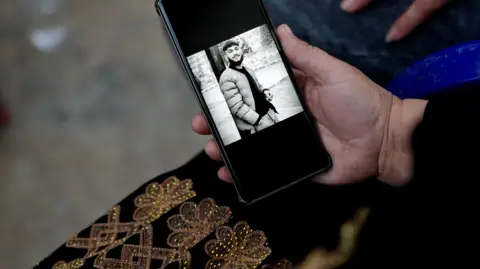 Goktay Koraltan/BBC Walid's mother holds out her phone showing a black and white image of him 