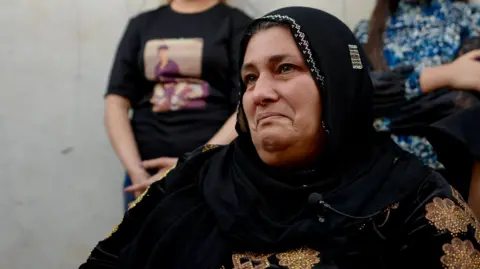 Goktay Koraltan/BBC Rojin Mohammed, wearing a black scarf around her head, tearing up 