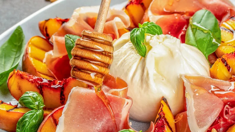 burrata with grilled peaches, prosciutto, basil and a wooden honey dipper.